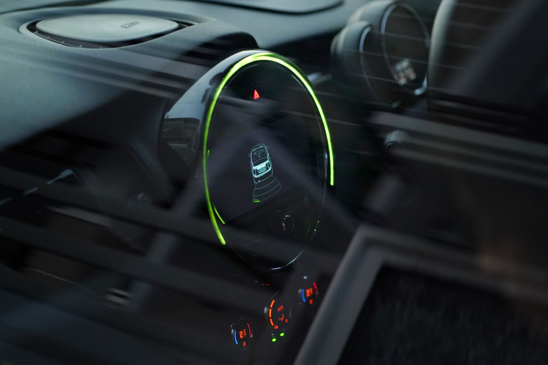 Écran de bord circulaire cerclé de lumière verte dans l’habitacle d’une voiture moderne.