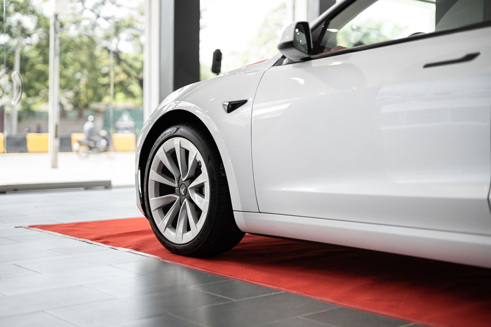 Flanc avant et roue d’une voiture électrique blanche stationnée sur un tapis rouge en salle d’exposition.