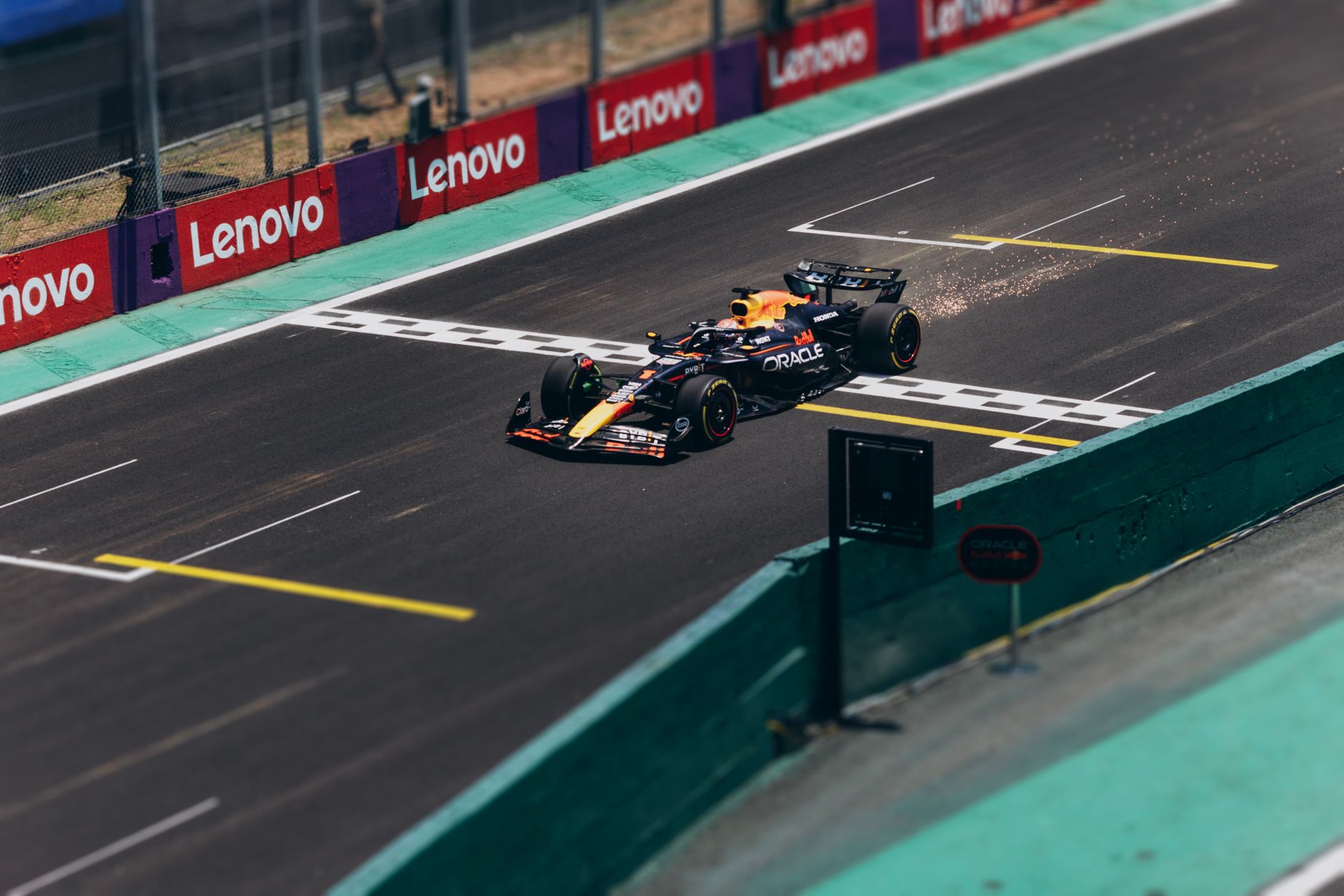 Une monoplace de course roulant sur un circuit automobile asphalté en longeant un muret bordé de panneaux publicitaires.